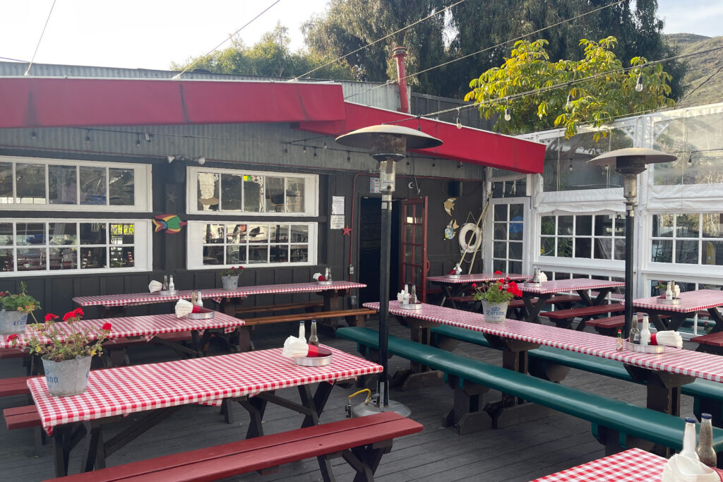 Photo of Reel Inn's wood decked outside patio dining area with picnic benches covered in red gingham table clothes 